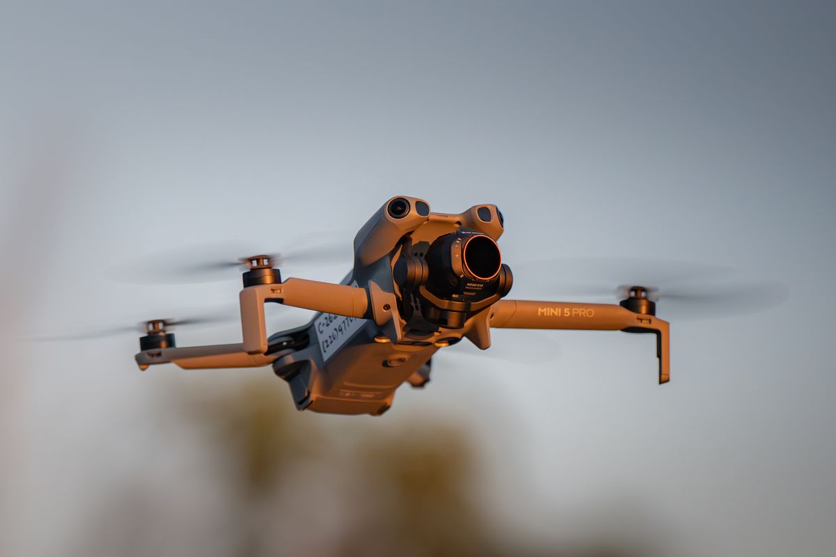 Side profile of the drone in flight against open sky, airframe marked with operator contact details